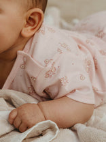 Close-up of a baby in a pink outfit with floral patterns, lying on a soft surface.